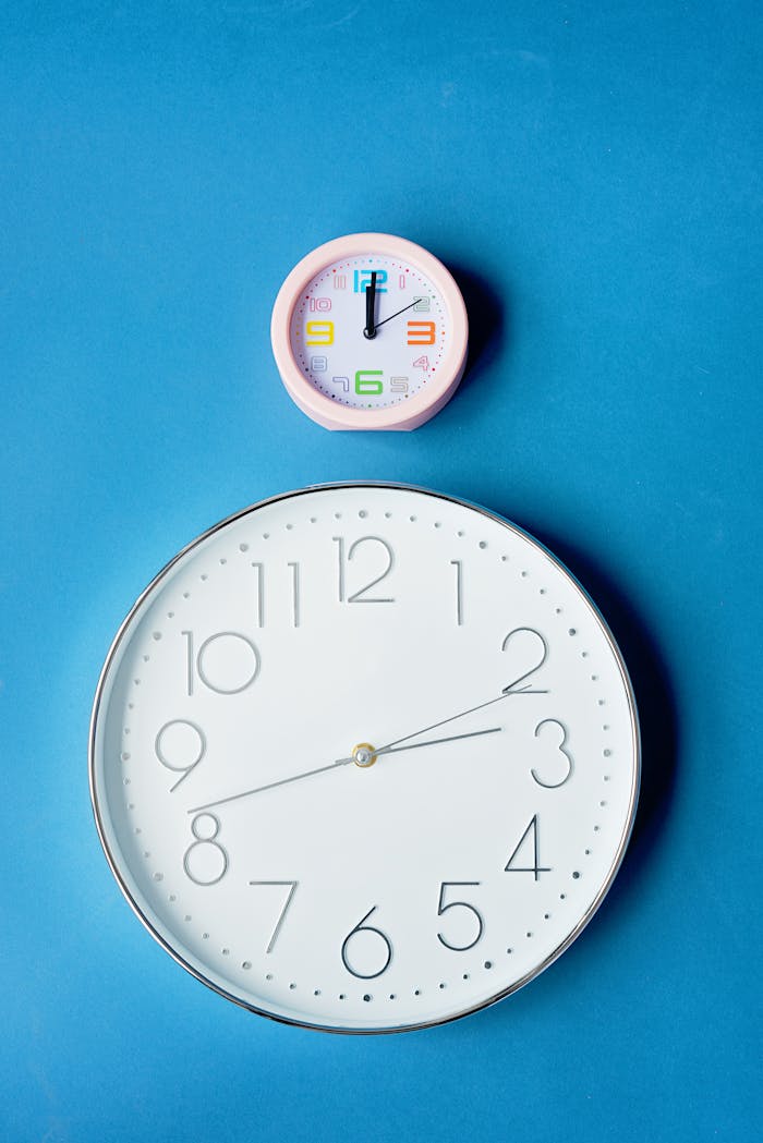 Close-up of large and small analog clocks on a blue surface.